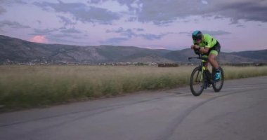 Profesyonel bir yarış bisikletine binen triatlon sporcusunun gece bisikleti eğitimi. Akşamları virajlı bir yolda sağlıklı ve yoğun bir egzersiz. Yavaş çekim izleme çekimi. 