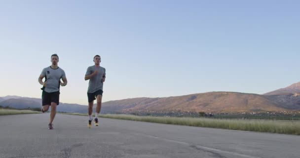 Dos hombres corren por la carretera rodeados de naturaleza — Vídeo de stock