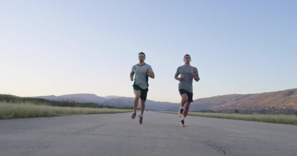 Dos hombres corren por la carretera rodeados de naturaleza — Vídeo de stock