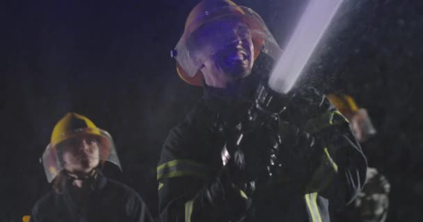 緊急時に炎と戦うために水を使用して消防士の男性と女性のグループ 夜間訓練の消防車の近くの耐火設備の消防チーム スローモーション — ストック動画