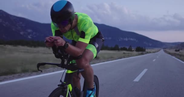 プロのレーシングバイクに乗ってトライアスロン選手の夜の自転車トレーニング 夕方には曲がりくねった田舎道で健康的な強烈なワークアウト スローモーショントラッキングショット — ストック動画