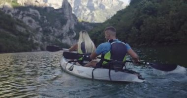 Kano yavaş çekimde kürek çekiyor. Kanocu kadın ve erkek arkadaşlarıyla güzel bir arazide kayak yapıyor. Kayakçılar gölde bir kanoyla spor yapıyorlar. Yaz boyunca su sporları. Yüksek kalite 4k görüntü