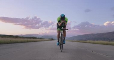 Profesyonel bir yarış bisikletine binen triatlon sporcusunun gece bisikleti eğitimi. Akşamları virajlı bir yolda sağlıklı ve yoğun bir egzersiz. Yavaş çekim izleme çekimi. 
