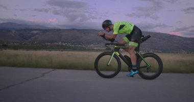 Profesyonel bir yarış bisikletine binen triatlon sporcusunun gece bisikleti eğitimi. Akşamları virajlı bir yolda sağlıklı ve yoğun bir egzersiz. Yavaş çekim izleme çekimi. 