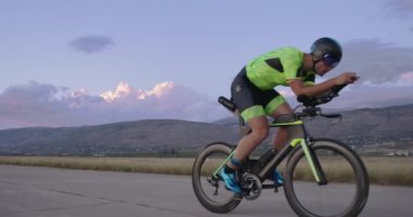 Triatlon atleti, gece spor yaparken virajlı bir kır yolunda profesyonel bir yarış bisikleti sürüyor. 