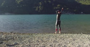 Dalgıç kıyafetli profesyonel triatlon sporcusu demir adam yarışması için yüzme antrenmanına bir gölün su sıçratan sularında koşup zıplayarak başlıyor. Yavaş çekim izleme çekimi. 
