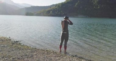 Dalgıç kıyafetli profesyonel triatlon sporcusu demir adam yarışması için yüzme antrenmanına bir gölün su sıçratan sularında koşup zıplayarak başlıyor. Yavaş çekim izleme çekimi. 