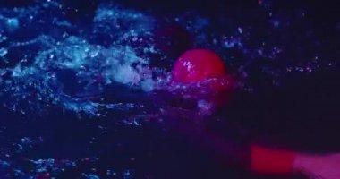 Triatlon atleti karanlık gecede yüzüyor. Dalış kıyafeti giyiyor.