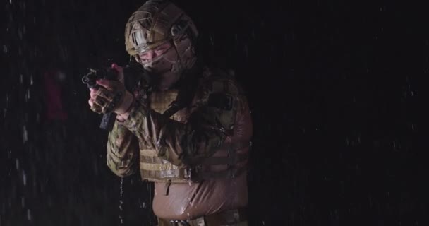 Close-up fortes gotas de chuva em soldado em camuflagem na noite, tomando ação militar, mirando mira arma, e olhando em frente poderosamente e calmamente — Vídeo de Stock