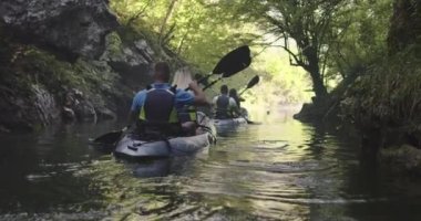 Kano yavaş çekimde kürek çekiyor. Kanocu kadın ve erkek güzel bir manzarada kayak yapıyorlar. Kayakçılar arkadaşlarıyla gölde bir kanoyla spor yapıyorlar. Yaz boyunca su sporları.