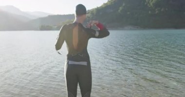 Dalgıç kıyafetli profesyonel triatlon sporcusu demir adam yarışması için yüzme antrenmanına bir gölün su sıçratan sularında koşup zıplayarak başlıyor. Yavaş çekim izleme çekimi. 