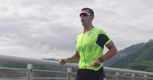 Тріатлон - чоловічий тріатлоніст, який біжить у тренувальному костюмі для залізних перегонів. Чоловік біжить бігаючи вранці . — стокове відео