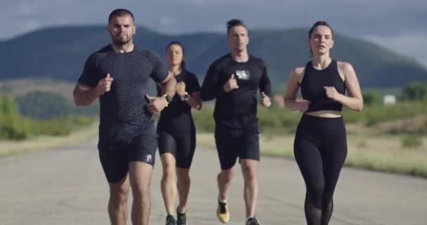 Wieloetniczna grupa sportowców biegających razem po panoramicznej wiejskiej drodze. Różnorodny zespół biegaczy na porannym treningu. — Wideo stockowe