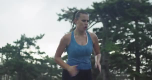 Zdjęcie śledzące młodą kobietę w sportowej odzieży biegającą przez wiecznie zielony las na wiejskiej drodze. — Wideo stockowe