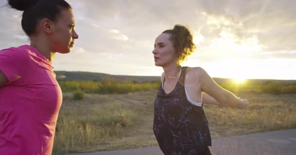 Two multi-ethnic girls stretching together in the street, stretching their legs before a run. — Vídeos de Stock