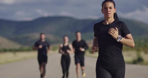 Grupo multiétnico de atletas correndo juntos em uma estrada panorâmica do campo. Equipe diversa de corredores no treinamento matinal. — Vídeo de Stock