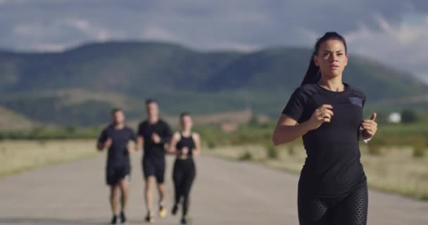 Grupo multiétnico de atletas corriendo juntos en una carretera panorámica del campo. Equipo diverso de corredores en el entrenamiento matutino. — Vídeos de Stock