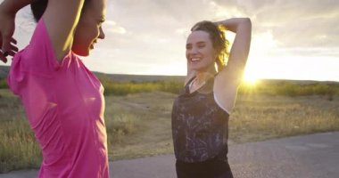 İki çok ırklı kız sokakta birlikte koşuya çıkmadan önce bacaklarını esnetiyorlar..