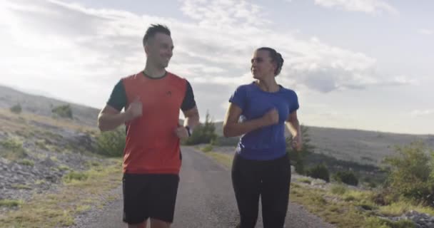 Tracking slow motion shot of sportive couple jogging outdoors in the morning, trail running experience in nature. Healthy lifestyle concept. — Stock Video