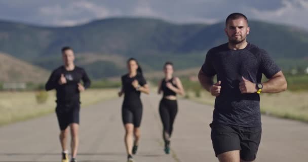 Многонациональная группа спортсменов бегает вместе по панорамной сельской дороге. Разнообразная команда бегунов на утренних тренировках. — стоковое видео
