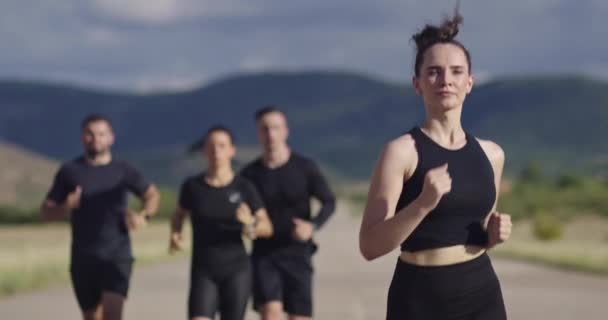 Grupo multiétnico de atletas corriendo juntos en una carretera panorámica del campo. Equipo diverso de corredores en el entrenamiento matutino. — Vídeos de Stock