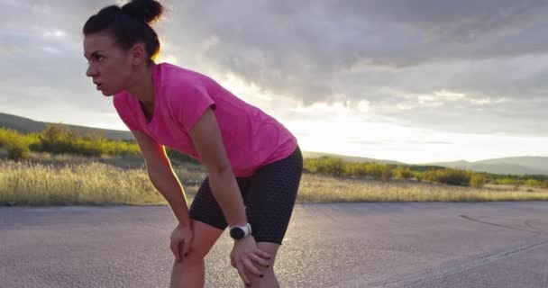 Fit en actieve jonge vrouw nemen een pauze van joggen. Moe renner die 's nachts op adem komt op straat. 4k — Stockvideo