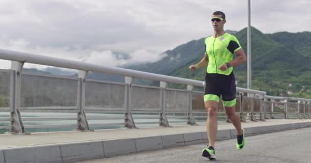 Triatlón: triatleta masculino que corre en el entrenamiento del traje de triatlón para la carrera de Ironman. Hombre corredor ejercitando jogging en la mañana. — Vídeo de stock