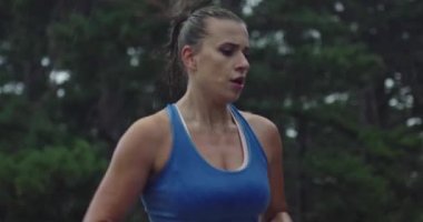 Ağır çekimde, spor giysili genç bir kadının, yağmur altındaki bir kır yolunda, yemyeşil bir ormanda koşarkenki görüntüsü..