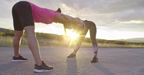 Two multi-ethnic girls stretching together in the street, stretching their legs before a run. — ストック動画