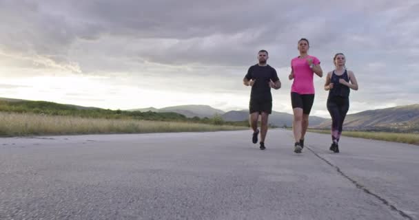 Grupo multiétnico de atletas corriendo juntos en una carretera panorámica del campo. Equipo diverso de corredores en el entrenamiento matutino. — Vídeos de Stock