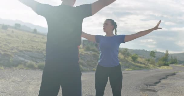 Couple of determined athletes stretching together, warming up and preparing for running training on a panoramic road. — Vídeos de Stock