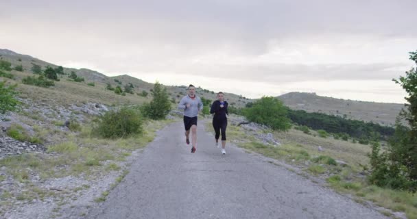 Seguimiento de la toma de cámara lenta de la pareja deportiva corriendo al aire libre en la mañana, la experiencia de trail running en la naturaleza. concepto de estilo de vida saludable. — Vídeos de Stock