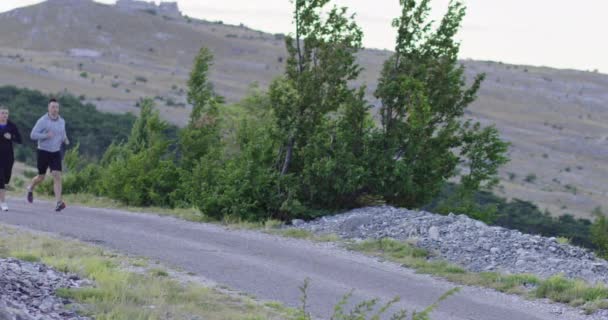 Seguimiento de la toma de cámara lenta de la pareja deportiva corriendo al aire libre en la mañana, la experiencia de trail running en la naturaleza. concepto de estilo de vida saludable. — Vídeo de stock