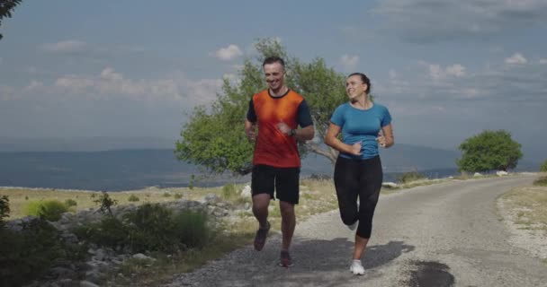 Rastreamento tiro em câmera lenta de casal esportivo correndo ao ar livre pela manhã, experiência de corrida de trilha na natureza. Conceito de estilo de vida saudável. — Vídeo de Stock