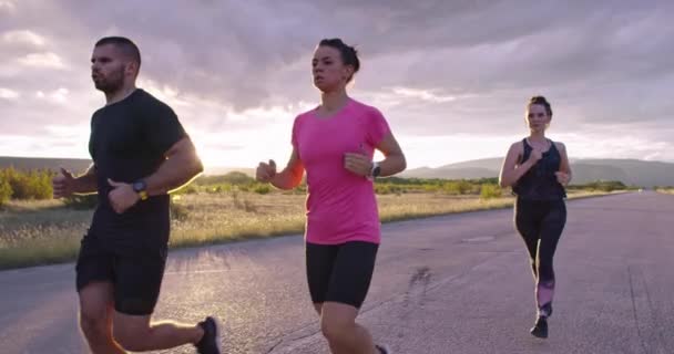 Grupo multiétnico de atletas corriendo juntos en una carretera panorámica del campo. Equipo diverso de corredores en el entrenamiento matutino. — Vídeo de stock