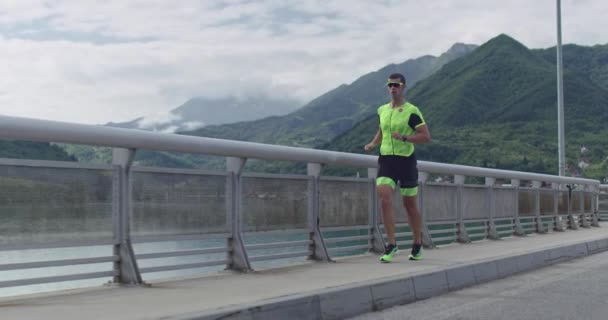 Triatlón: triatleta masculino que corre en el entrenamiento del traje de triatlón para la carrera de Ironman. Hombre corredor ejercitando jogging en la mañana. — Vídeo de stock