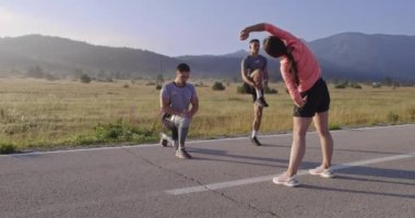 Çeşitli atletler sabah koşusuna hazırlanırken panoramik bir yolda esneyip ısınıyorlar. Yüksek kaliteli görüntüler. Seçici odak.