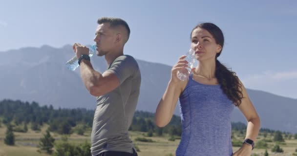 Zpomalený záběr páru běžců, kteří pijí vodu, odpočívají po intenzivním tréninku v přírodě. Kvalitní 4K záběry. Selektivní zaměření.