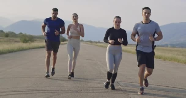 パノラマの田舎道で一緒に実行している選手の多民族グループ 朝のトレーニングでジョギングの多様なチーム 高品質の映像 スローモーション追跡ショット 選択的焦点 — ストック動画