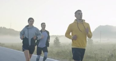 Panoramik bir kırsal yolda birlikte koşan çok ırklı bir grup sporcu. Çeşitli koşu takımları sabah antrenmanında. Yüksek kaliteli görüntüler. Yavaş çekim takip çekimi. Seçici odak. 