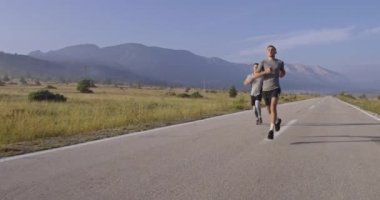 Panoramik bir kırsal yolda birlikte koşan çok ırklı bir grup sporcu. Çeşitli koşu takımları sabah antrenmanında. Yüksek kaliteli görüntüler. Yavaş çekim takip çekimi. Seçici odak. 