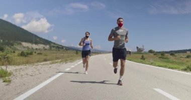 Bir salgın sırasında yolda koşan tıbbi maskeli bir çift. Spor ve koronavirüs. Covid-19. Korunma. Sağlık konsepti. Sosyal uzaklık. Yavaş çekim takip çekimi. Seçici odak. 