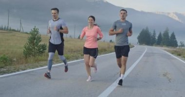 Panoramik bir kırsal yolda birlikte koşan çok ırklı bir grup sporcu. Çeşitli koşu takımları sabah antrenmanında. Yüksek kaliteli görüntüler. Yavaş çekim takip çekimi. Seçici odak. 