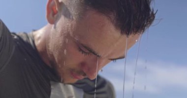 Genç sporcu, sıcak bir yaz gününde parkta yoğun bir idmandan sonra kendini suyla tazeler. Yüksek kaliteli görüntüler. Yavaş çekim.