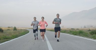 Panoramik bir kırsal yolda birlikte koşan çok ırklı bir grup sporcu. Çeşitli koşu takımları sabah antrenmanında. Yüksek kaliteli görüntüler. Yavaş çekim takip çekimi. Seçici odak. 