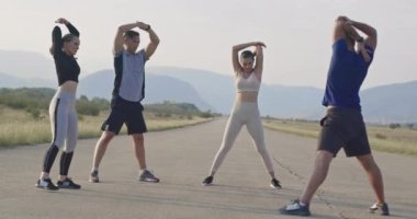 Çok ırklı bir grup sporcu panoramik bir yolda birlikte esniyorlar. Yüksek kaliteli görüntüler