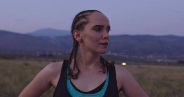 Formda ve aktif genç bir kadın sabah ya da akşam koşuya ara veriyor. Şehir sokağında akşamları soluklanan yorgun koşucu. Yüksek kalite 4K görüntü. Yörüngede yavaş çekim. 