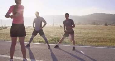 Çeşitli atletler sabah koşusuna hazırlanırken panoramik bir yolda esneyip ısınıyorlar. Yüksek kaliteli görüntüler. Seçici odak.