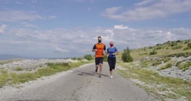 Bir salgın sırasında yolda koşan tıbbi maskeli bir çift. Spor ve koronavirüs. Covid-19. Korunma. Sağlık konsepti. Sosyal uzaklık. Ağır çekim. Seçici odak. 
