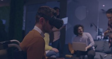 Modern açık uzay ofisinde çalışan engelli bir iş adamı sanal gerçeklik gözlüğü ve İHA simülasyonu kullanarak takım toplantısı yapıyor. Girişim işinde etkin takım çalışması.